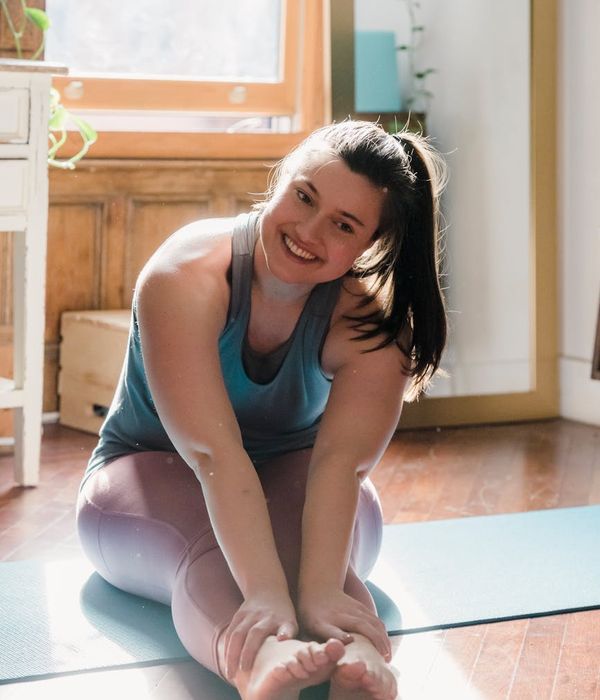 Woman smiling and stretching in a bright, sunlit room in the morning.